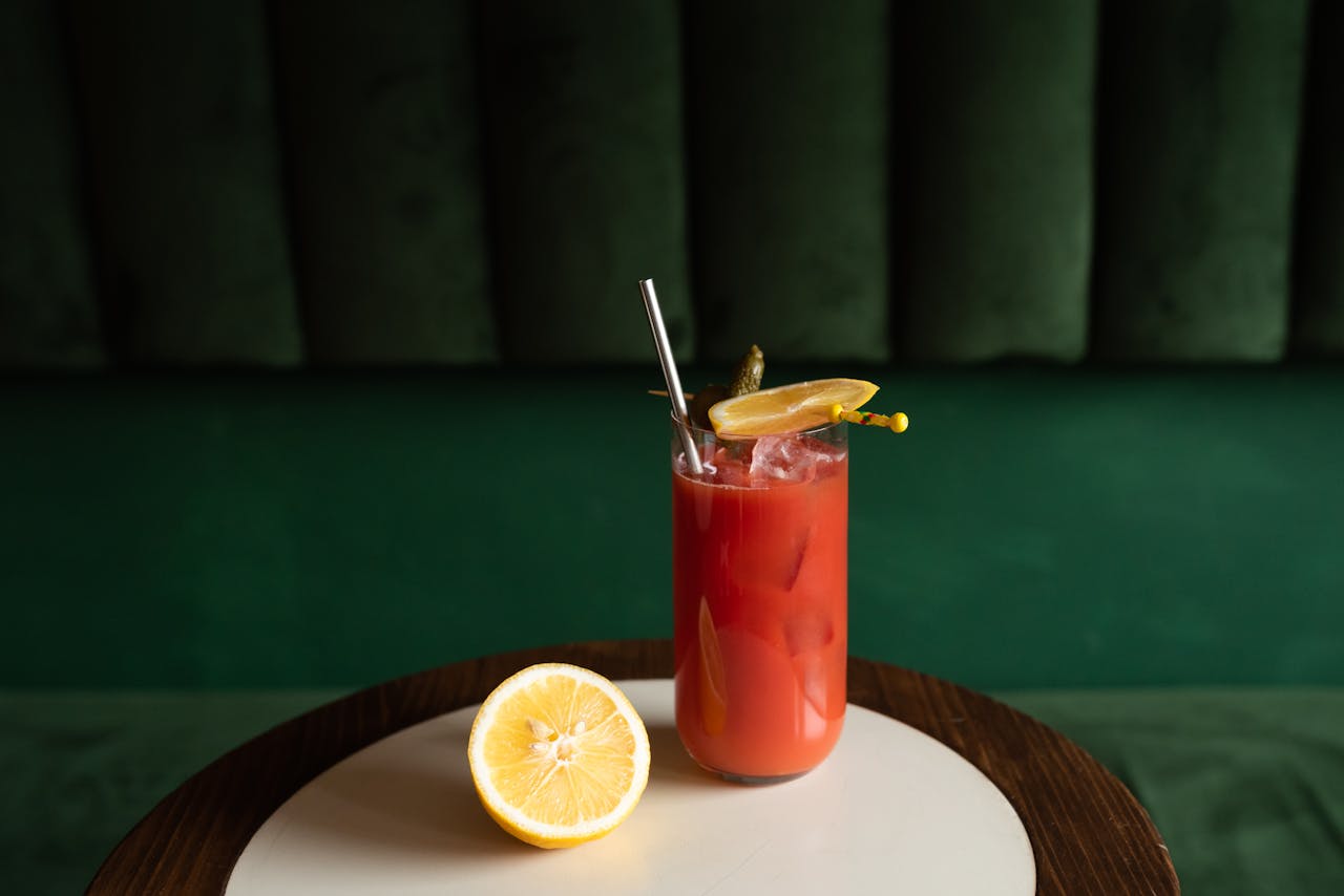 A refreshing red cocktail with lemon slices and a pickle garnish on a table.